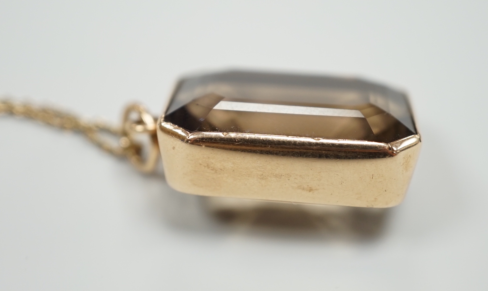 A yellow metal mounted smoky quartz pendant, 24mm, on a yellow metal fine link chain(a.f.), gross weight 15.6 grams.